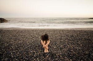 Young sad woman alone in a black stone beach.