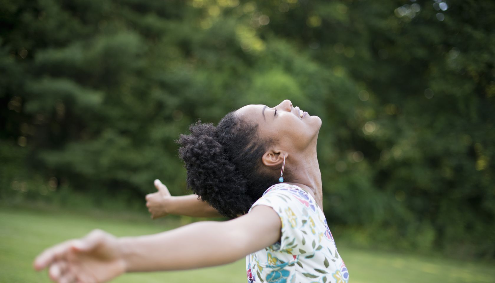 A young woman in a summer dress with her arms outstretched, celebrating freedom.