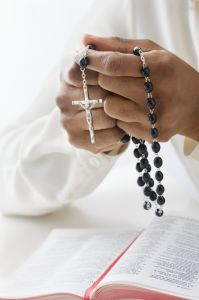Woman holding rosary over bible, close-up of hands