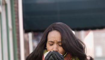 Woman sneezing on sidewalk