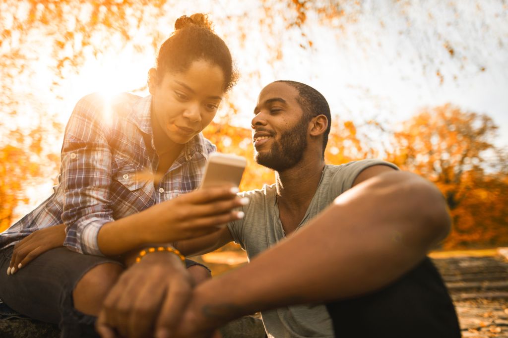 Young African American couple using smart phone during autumn day in nature.