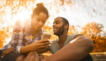 Young African American couple using smart phone during autumn day in nature.