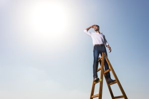 Happy African American businessman on the ladders against the sky.