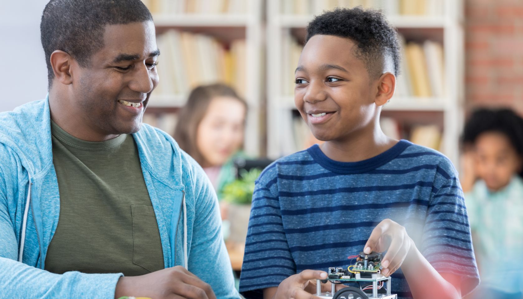 Male mentor and junior high student discussing robotics project and laughing