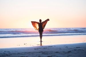 Young girl wearing butterfly wings and dancing on the beach at sunset