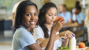 Teenager eating healthy lunch with friends in school lunchroom