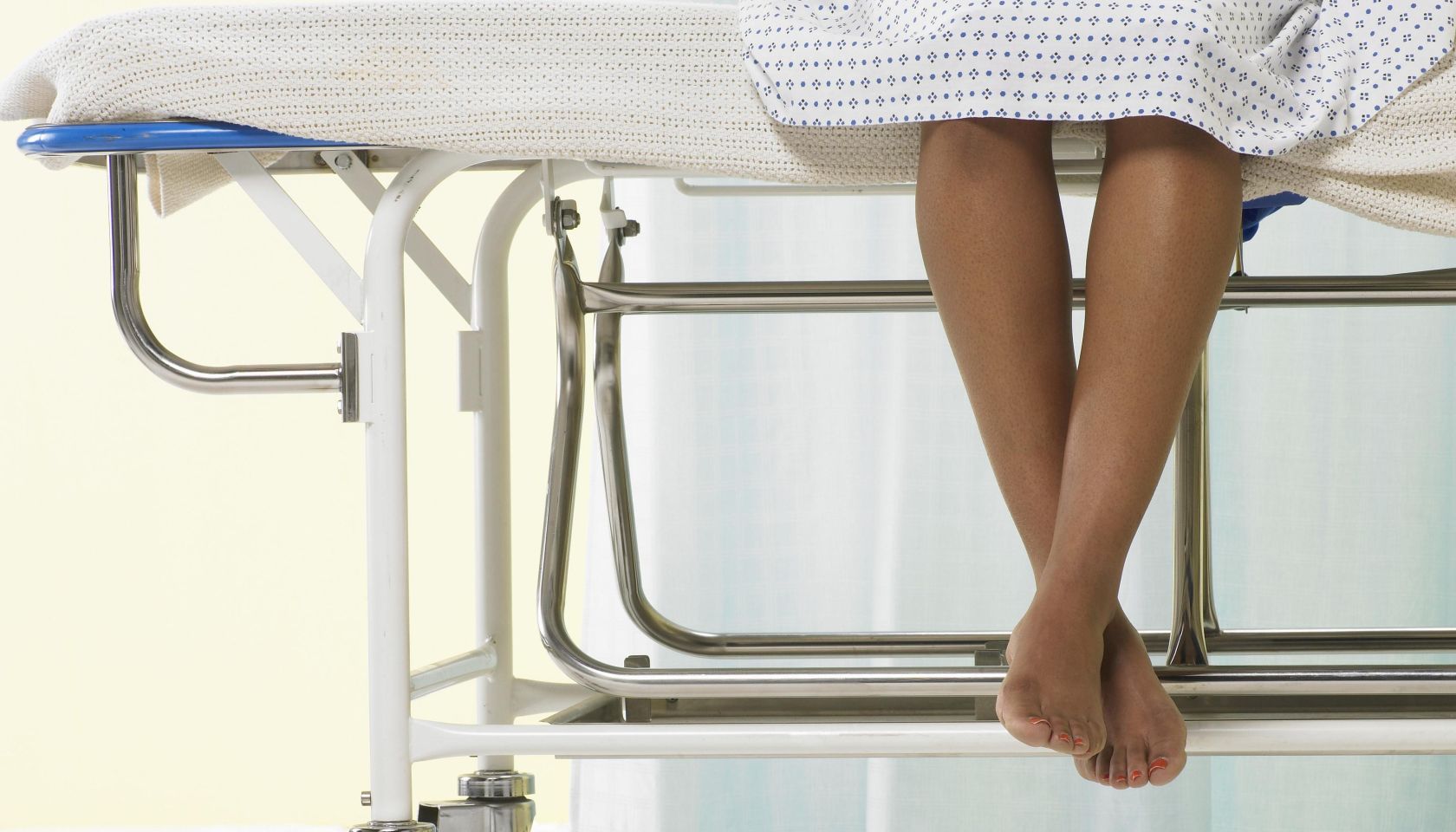 Female patient sitting on gurney in hospital gown, low section