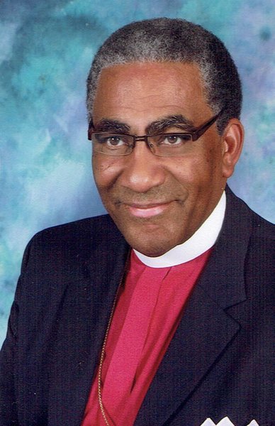 A portrait of a smiling African American man wearing a red clerical robe and glasses.