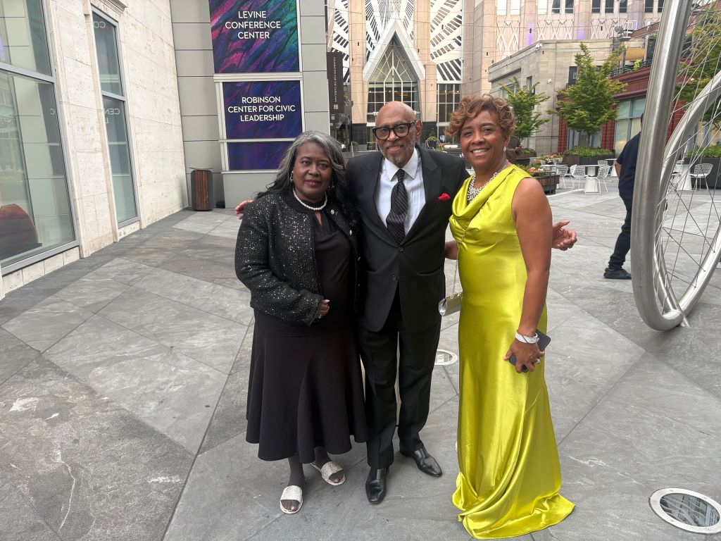 Three people posing for a photo in front of the Levine Conference Center and Robinson Center for Civic Leadership.