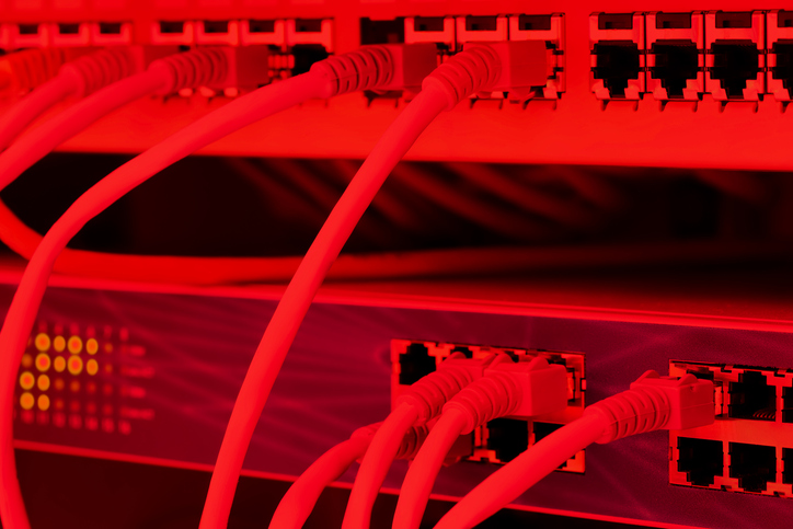 A network switch panel with several ethernet cables plugged into RJ45 ports red toned image